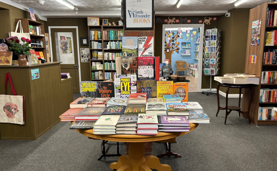 Table with books on display in front of image with a table further back and bookshelves on back wall