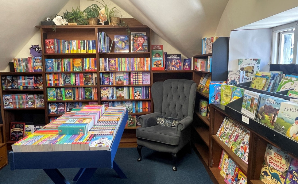 Display of books on shelves and table with armchair in corner